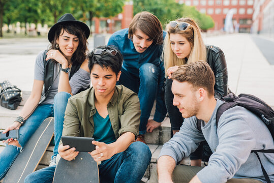 Group of young friends watching smartphone while sitting outdoors