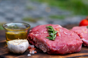 Raw meat beef steak organic fresh ingredient on wooden board table background in kitchen with rosemary, salt, garlic, tomato, black pepper, olive oil. Meat beef on wooden plate for beefsteak raw meat