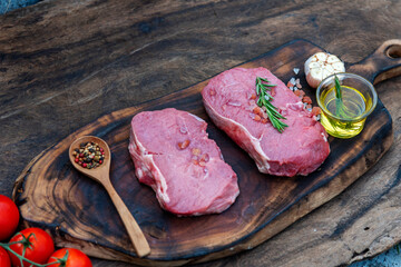 Raw meat beef steak organic fresh ingredient on wooden board table background in kitchen with rosemary, salt, garlic, tomato, black pepper, olive oil. Meat beef on wooden plate for beefsteak raw meat