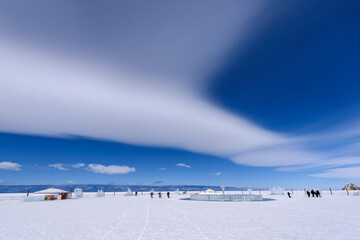 Silhouette of men ride bicycle near yurt and ice figures on the frozen lake Baikal in sunny weather with beautiful clouds sky