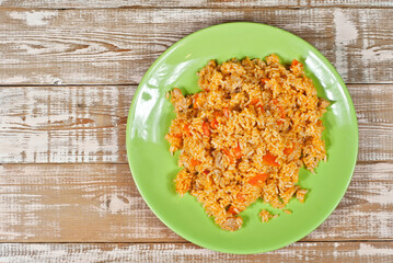 Pilaf with meat and carrots in a green plate. Rice on a pink shabby board. Place for text and copy space near food.