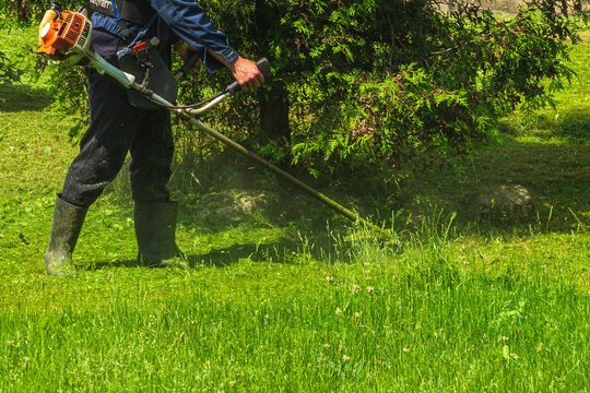 A man mows the grass with a gasoline scythe