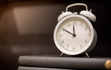 Naklejka premium Classic white clock on the pile of books on the wooden backdrop for show the timing of life and time is important concept.