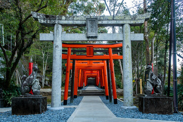 Row of red torii gates with two stone statues of guardian foxes on the sides in Suwa Shinto Shrine in Nagasaki, Japan. - Powered by Adobe