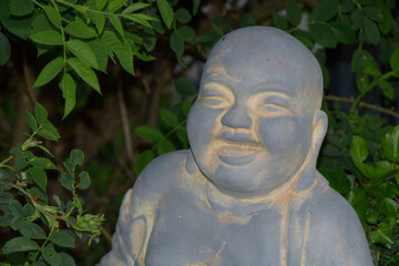 portrait of a smiling stone buddha in a green rosebush