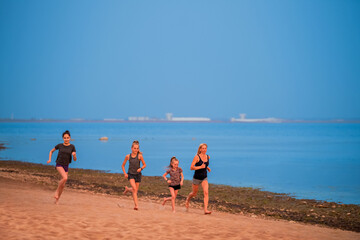 Children and adult girls run along the coast in sportswear on a background of nature at sunset