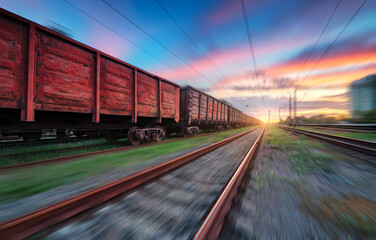 Moving freight train at sunset. Railroad and beautiful sky with clouds with motion blur effect in summer. Industrial landscape with train, railway station and blurred background.  Railway platform