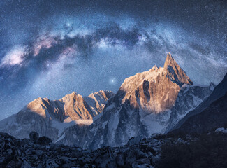 Arched Milky Way over the beautiful mountains at night in Himalayas, Nepal. Colorful space landscape with blue starry sky with Milky Way arch, snowy mountain peak. Galaxy, stars and rocks. Nature