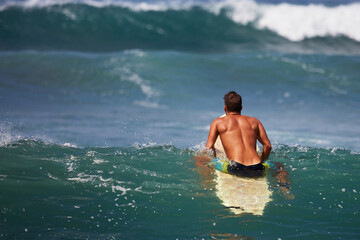 young man surfer sitting on surfboard on wave