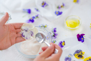 The chef's hands are holding a violet pansy flower in their hands and pour sugar on it with a...
