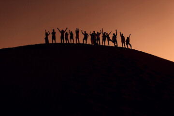 People standing on top of dune in desert with hands up. Silhouettes at sunset.