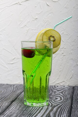 Green lemonade in a glass. Garnished with a slice of lemon and kiwi. With a straw for a cocktail.