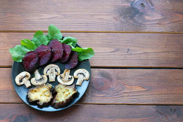 Fried vegetables on a plate on a wooden background. Vegetarian dish of beetroot, mushrooms and eggplant.