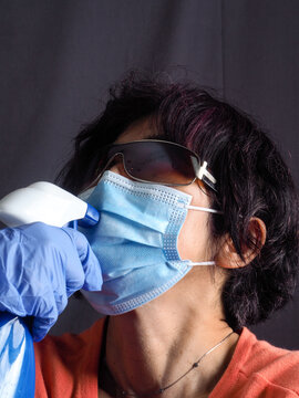 Funny Humorous Adult Asian 40s 50s Woman Wearing Protection Surgical Face Mask , Blue Latex Gloves, And Sun Glasses Pointing The Head With Blue Sanitizer Cleaning  Bottle As A Weapon 
