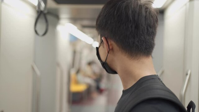 Asian young male standing inside subway sky train rail ride, talking on the phone during covid-19 pandemic, new normal concept on public transportation, social distance, risk of infectious disease