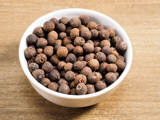Spice allspice in white bowl on brown wood background