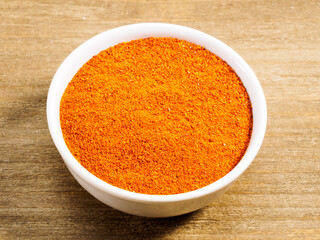 Spice red chili powder in white bowl on brown wood background