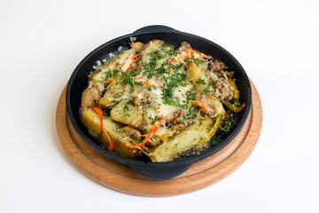 Dish on a black pan, which stands on a wooden stand. Baked potatoes with meat red and yellow pepper. Sprinkled with green parsley.