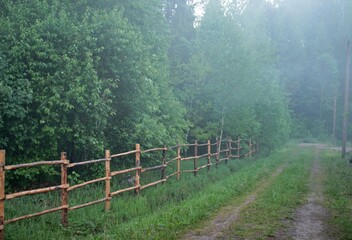 countryside road with fog in the evning.Village landscape with summer forest, wooden fence and mist.