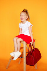 Young girl in red skirt having fun in studio yellow background. Studio portrait of young funny girl. White blonde little stylish fashion woman. Smiling child. yoth juvenile	in white shirt
