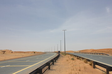 Modern asphalt highway passes through arid desert sand dunes terrain in Sharjah emirate in the United Arab Emirates.  