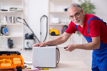 Old male contractor repairing microwave indoors