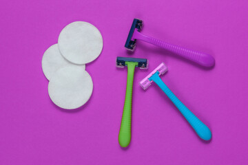 Beauty still life, minimalism. Many Plastic epilator razors with cotton circles on purple background. Women's accessories for beauty care. Top view