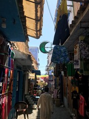 Naklejka premium Chefchaouen, Morocco - July 29, 2019: A man walks past the handicraft stalls of the blue-painted alleys of the Medina.