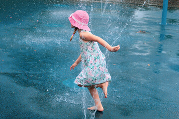 Young girl running through splash pad sprinkler wearing dress. © Yves