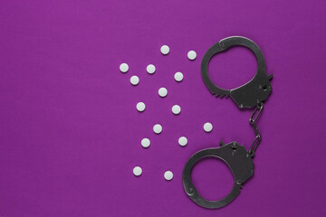 The concept of corruption in medicine. Pills and handcuffs on  purple background. Medical still...