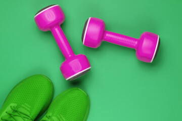 Minimalistic sport still life. Sports outfit. Sports shoes for training and plastic dumbbell on green background. Top view