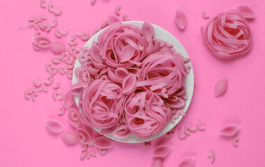 Different types of raw italian pasta in plate on pink background. Top view.
