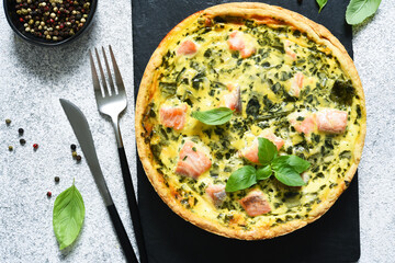 Pie (quiche) with salmon, spinach and cheese on a stone board on a concrete background. View from above.