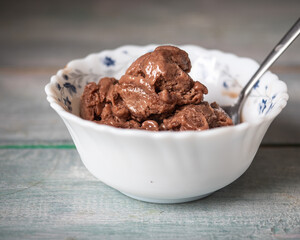 Chocolate ice cream in a small white plate with a floral print with a spoon o