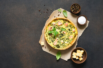 Quiche (pie) with salmon, spinach and soft cheese on a dark concrete background. View from above.