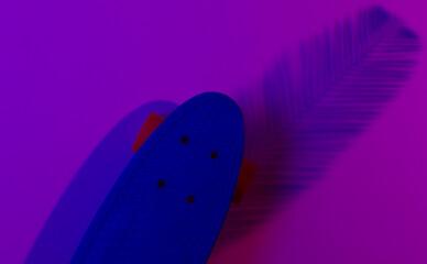 Plastic mini cruiser board on background with shadow from palm leaves. Neon gradient ligh. Top view