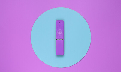 Modern tv remote in the middle of pink background with blue circle. Top view