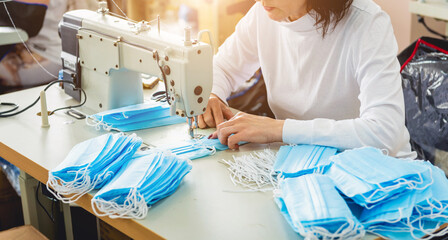 Woman sew the facial medical at sewing machine. Coronavirus pandemia.
