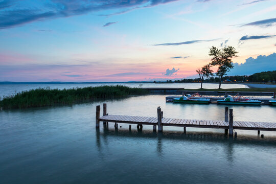 Wooden piers in the town of Podersdorf on Lake Neusiedl in Austria. In the background is a dramatic sunset sky.