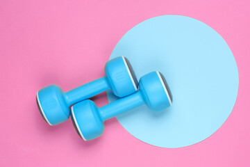 Plastic dumbbell on pink background with blue pastel circle. Top view. Minimalistic sport concept....