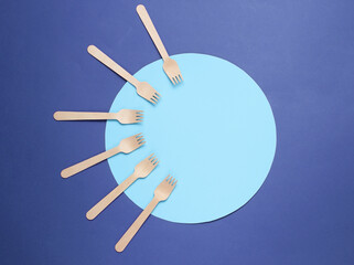 Eco friendly wooden forks on purple background with blue circle. Top view, minimalism