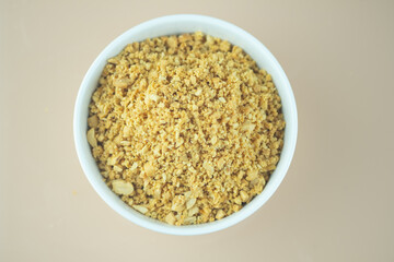Bowl of roasted crushed peanuts on white background.