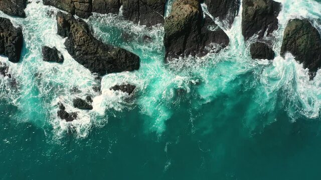 Aerial top view 4k footage by drone of ocean blue waves break on high cliff of a rocky mountain. Danger sea waves on a beach