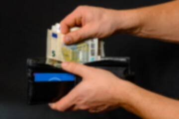 Man hand pulling money from wallet, black background and black wallet. Blurred and defocused image.