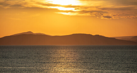 Fototapeta premium Sunrise, sunset clouds. Twilight, dusk cloudy sky over sea water, mountain silhouette