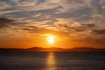 Sunrise, sunset clouds. Twilight, dusk cloudy sky over sea water, mountain silhouette