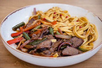 Italian spaghetti pasta with beef and bean pods, carrots in a deep plate on a wooden table in a restaurant.