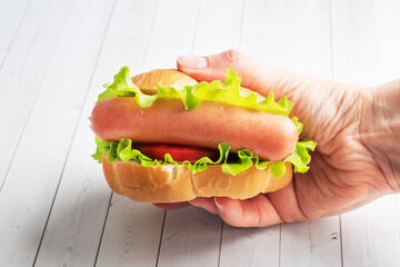 Hot dog with lettuce tomato and sausage hold in hands.
