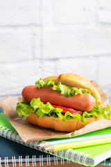 Hot dog with lettuce tomato and sausage. Notebooks and stationery. concept school Breakfast. Copy space.