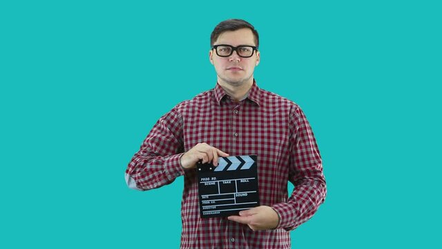 A man dressed in a plaid shirt and glasses holds a movie clapper in his hands.